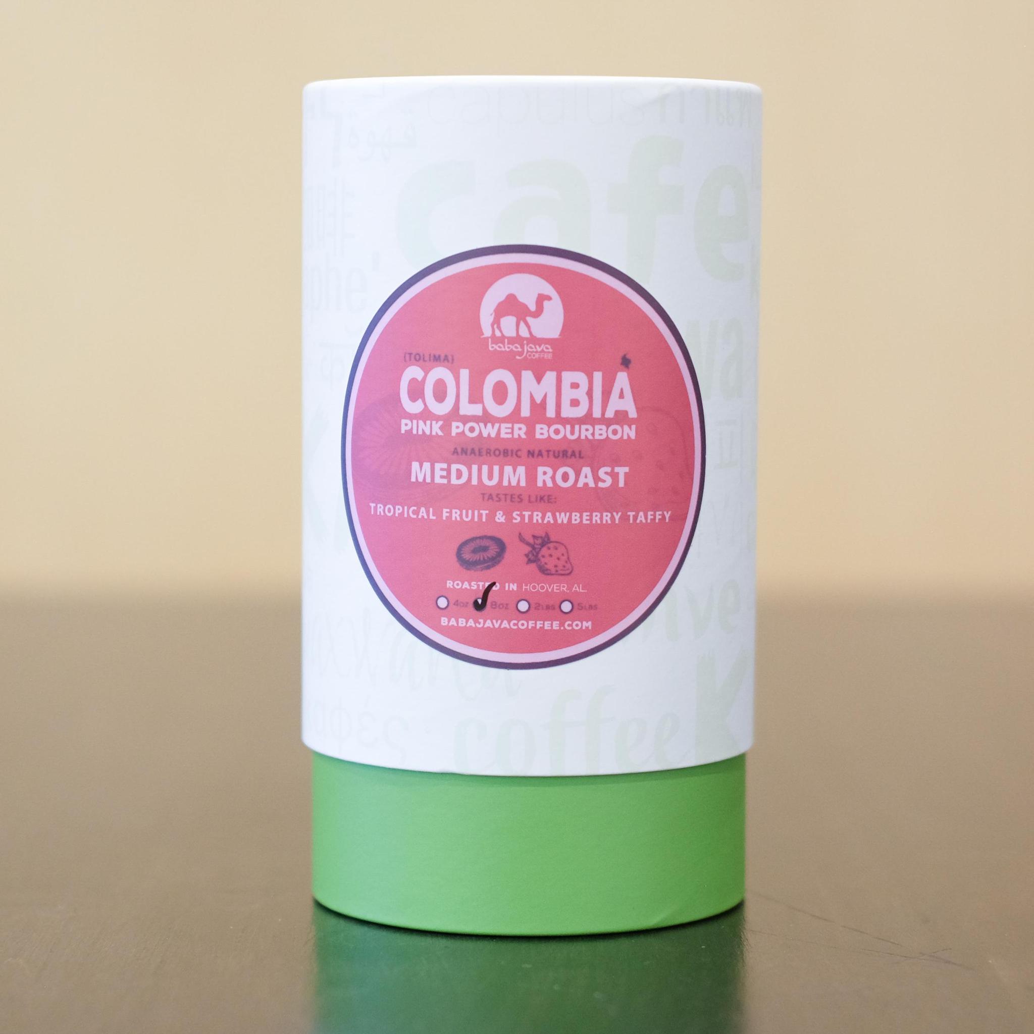 A tube of coffee with a pink label that reads Colombia Pink Power Bourbon. The tube has a the words coffee in various languages.