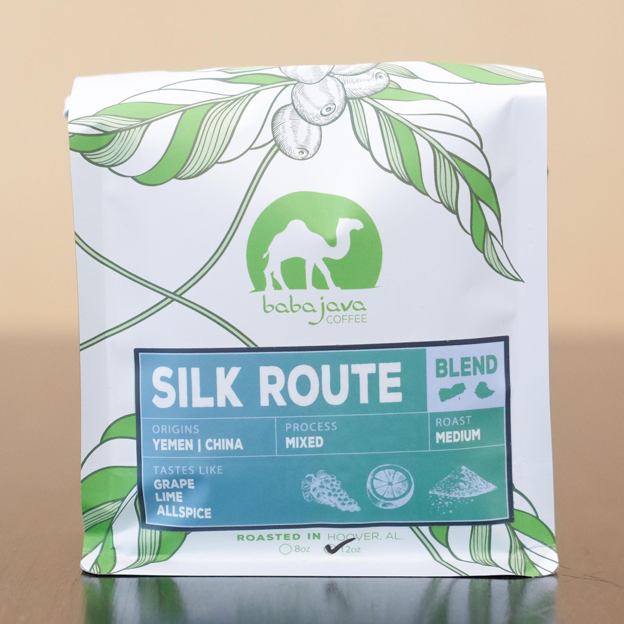A bag of coffee with a blue-green label that reads Silk Route. The bag has a drawing of a coffee plant and the Baba Java Coffee logo.